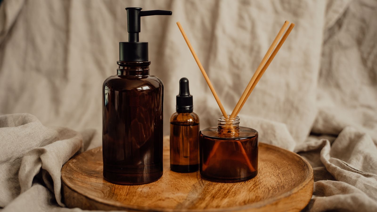 Amber glass diffuser bottle and small dropper bottles arranged on a wooden tray with linen.