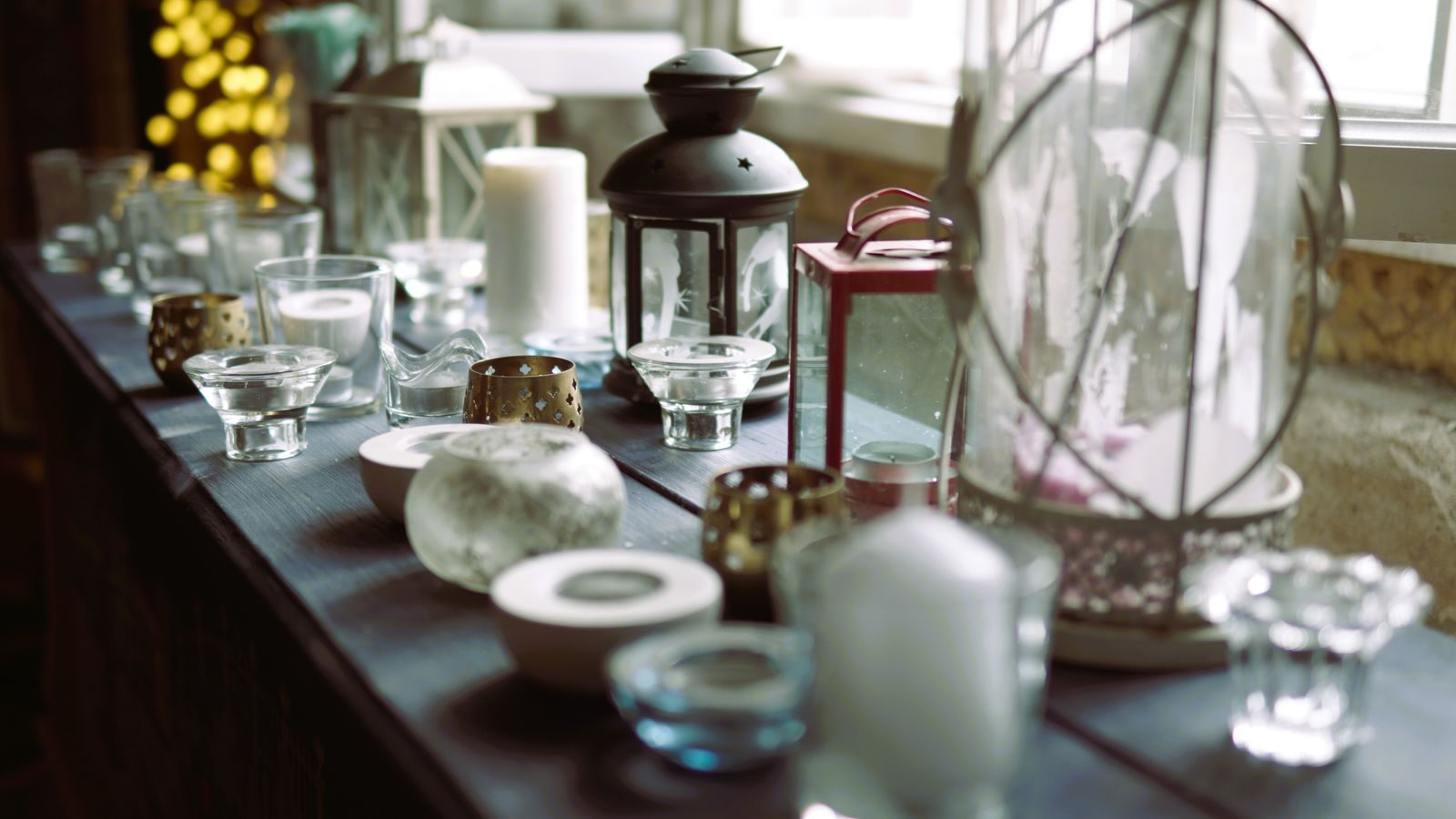 Long wooden table set with a mix of clear glass, tealight and pillar candle vessels.