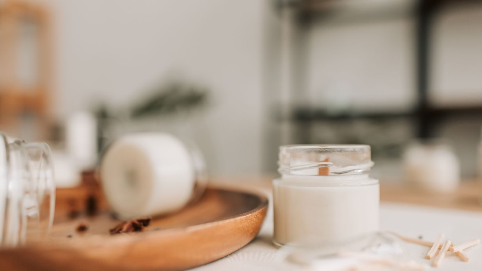 Soft-focus shot of a small white jar candle on a wooden tray with star anise.