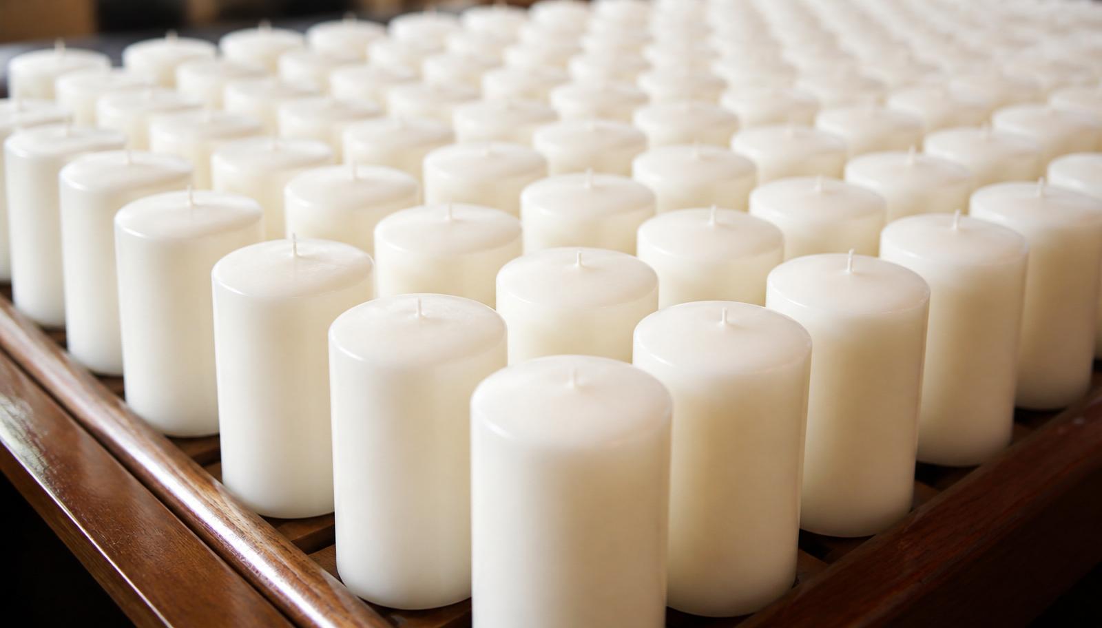 Hundreds of identical white paraffin pillar candles cooling on a wooden rack.