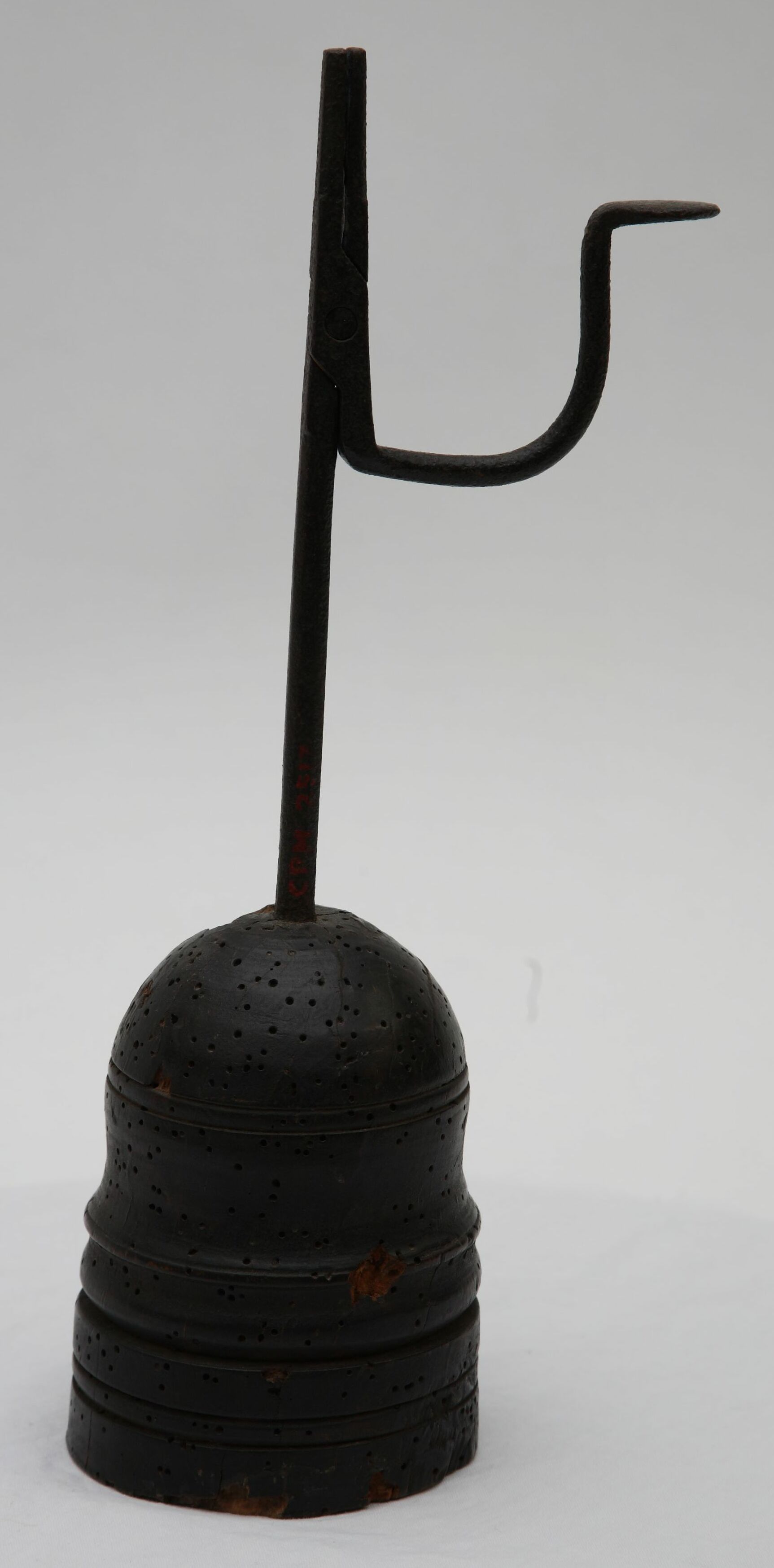 A simple iron rushlight holder gripping a thin reed dipped in fat, the earliest form of candle.