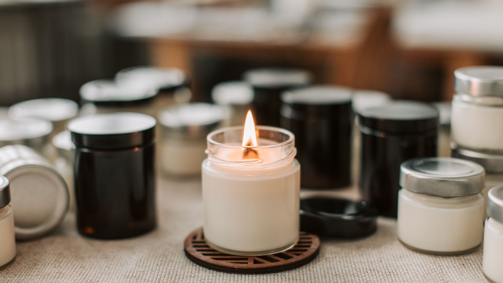 Rows of brown apothecary jar candles in soft daylight, with one lit candle in front.