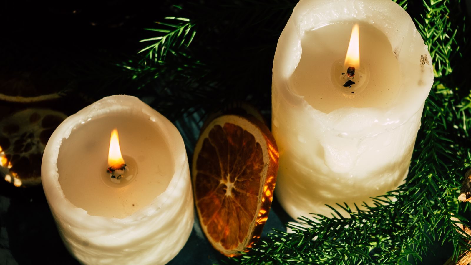 Cluster of pillar candles with dried orange slices and pine sprigs in warm winter light.