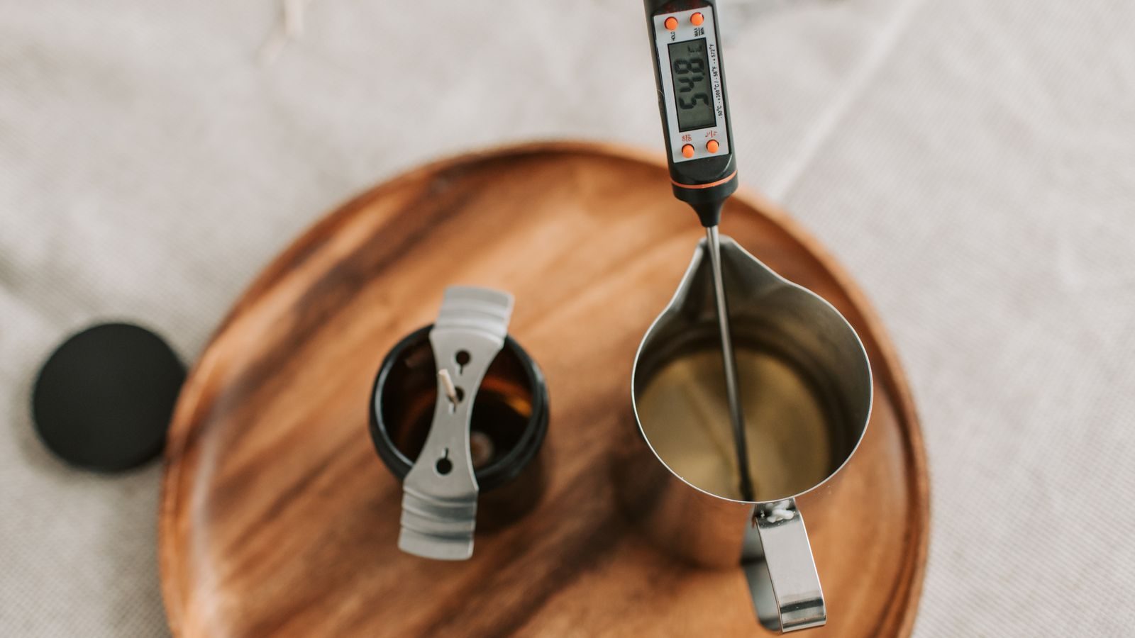 Wooden tray with a pouring jug, digital thermometer and lid on a linen-covered worktop.