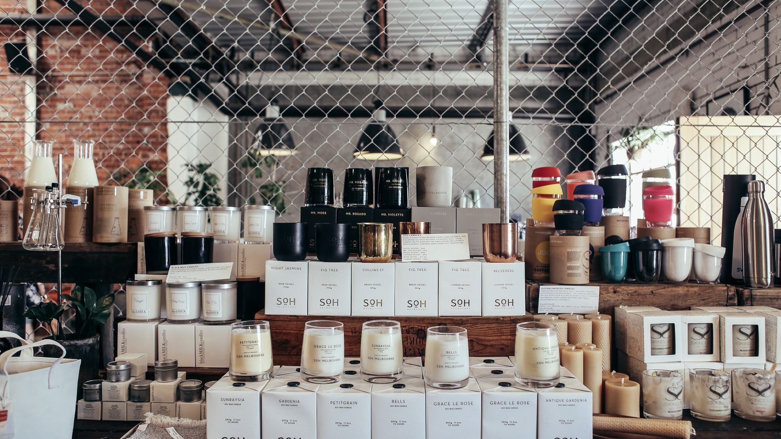 Retail shelves stacked with branded candle jars and pillar candles under industrial pendant lights.