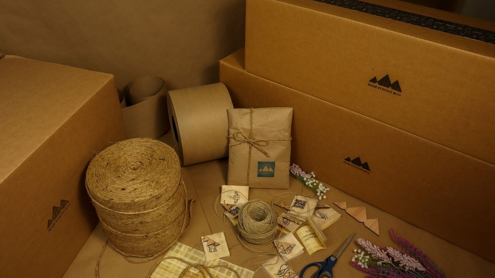 Cardboard shipping boxes with kraft-wrapped parcels, twine, scissors and dried lavender at the packing bench.