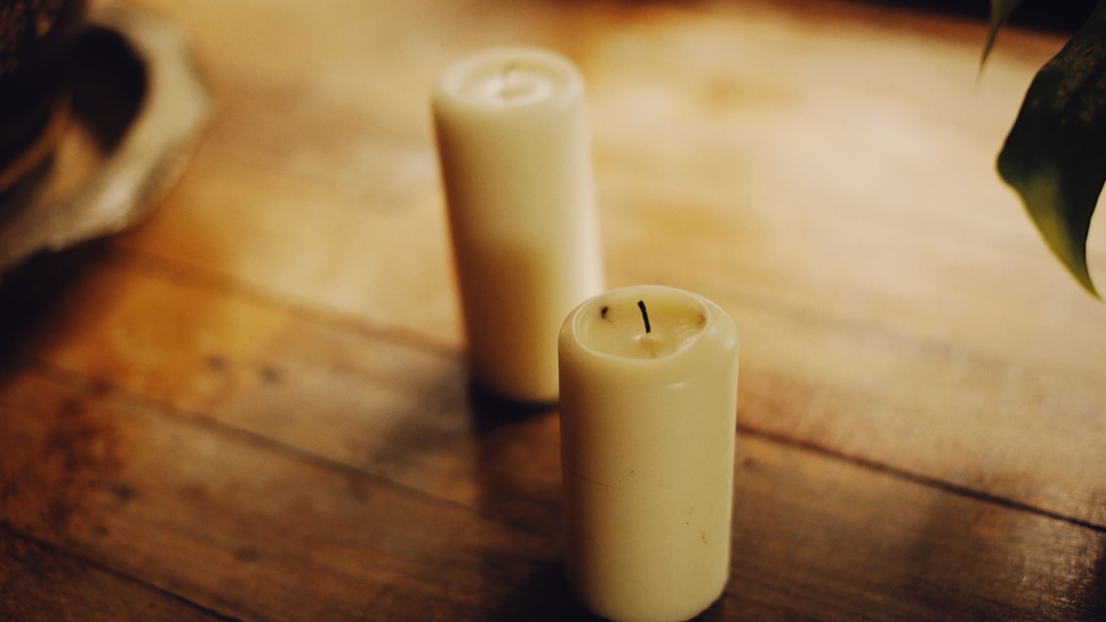 Cream pillar candle on a worn oak table in warm afternoon light.