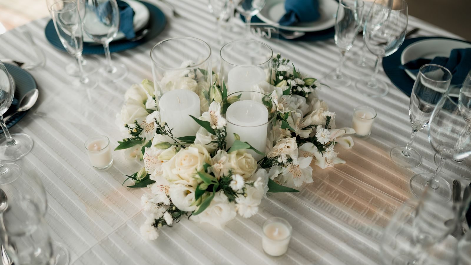 Long white table set with low candles and an ivory and green floral runner, glassware on either side.
